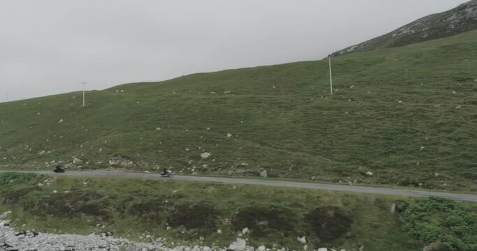 Drone panning shot of two motorbikes riding along the coastal road along the Scotland North Coast 500 route