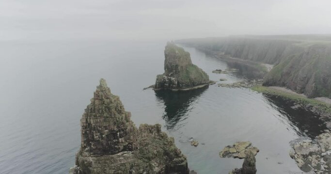 Slow drone panning across the sea showing the Stacks of Duncansby during misty and foggy weather along the Scotland North Coast 500 route at John O'Groats