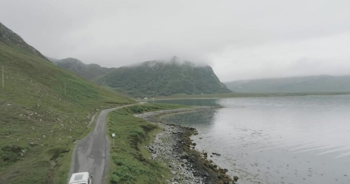 Close up drone tracking shot of a campervan on a single track road during a trip of the Scotland North Coast 500 with a Loch and cloudy topped mountains in view to passing the camper van