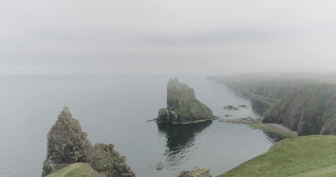 Slow drone panning across the shoreline showing the cliff edge and the Stacks of Duncansby during misty and foggy weather along the Scotland North Coast 500 route at John O'Groats