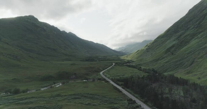 Dramatic wide drone shot showing the north coast 500 route which runs between two huge mountains with traffic flowing below and cloud cover in the background