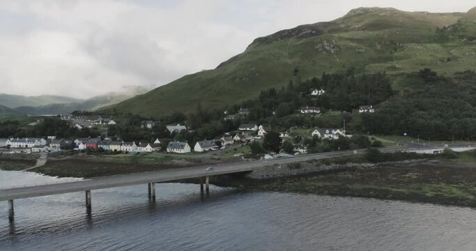 Panning drone shot tracking a car crossing the river Elchaig in Scotland showing the colourful village of Dornie in the background, scottish highlands