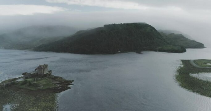 Wide drone shot showing Eilean Donan Castle, the sea and cloud covered mountains in the background shows the Scottish weather