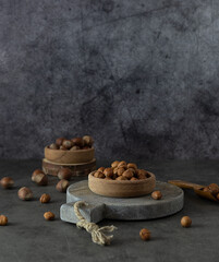 Peeled hazelnuts in a wooden bowl on a round stand. Nuts on the table. A wooden spoon in the background. Dark gray background, space for text