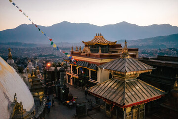 View of the golden top of the Swayambhu Stupa in Kathamndu Nepal after sunset. Colorful prayer flags wave against an purple evening sky.