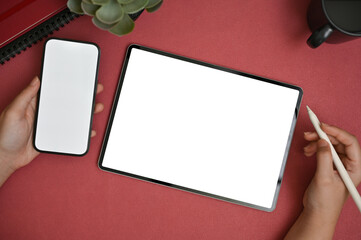 Obraz premium Top view of a female using her smartphone and her digital tablet on a red table.
