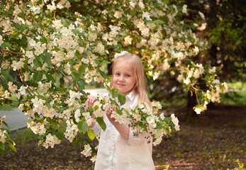 Smiling child poses outdoors. Childhood. Blonde girl poses near blooming apple tree. Spring.