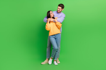 Full size photo of two cheerful lovely partners cuddle look each other isolated on green color...