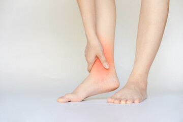 A woman's hand touches her red ankle due to an ankle injury caused by an accident.