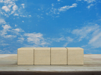 Four wood block cubes on wooden table over blue sky with white clouds