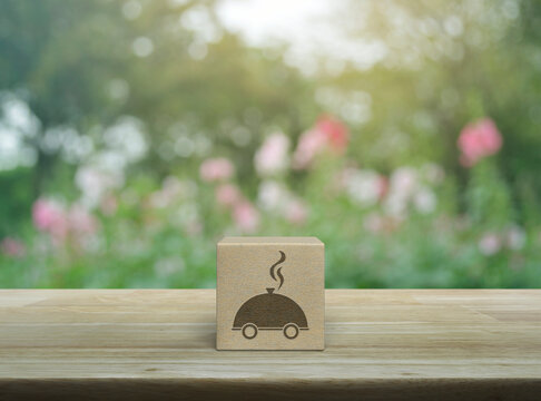 Restaurant cloche icon on wood block cube on wooden table over blur pink flower and tree in park, Business food delivery online concept