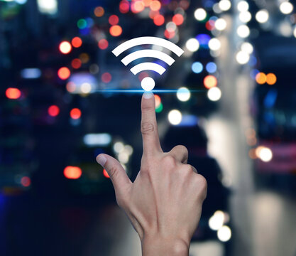 Hand pressing wi-fi icon over blur colourful night traffic jam road in city, Technology internet communication concept