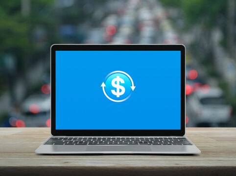 Money transfer icon on modern laptop computer screen on wooden table over blur of rush hour road in city, Business currency exchange online service concept