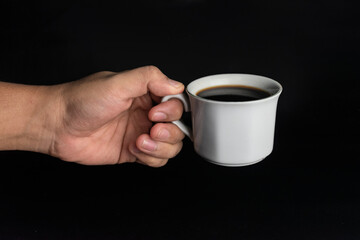man hand holding cup of black coffee isolated on black background
