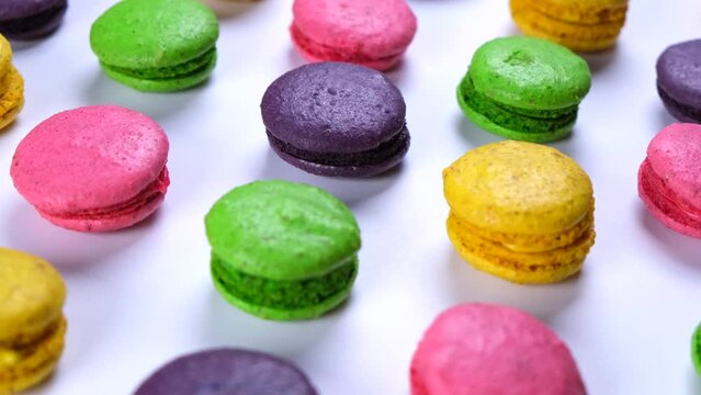 Rotating background of sweet macaroon cookies in different colors on a pink background