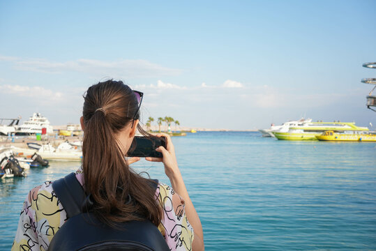 Young beautiful girl taking a picture of yachts at a docking bay in the sunset