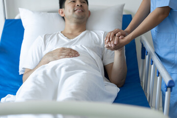 Physiotherapist giving advice and encouragement to male patient doing physiotherapy lying on...