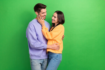 Portrait of two positive satisfied people cuddle hand touch face isolated on green color background