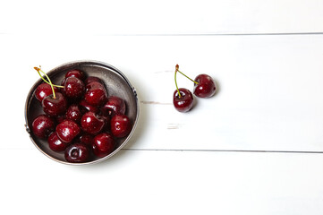 Obraz na płótnie Canvas Sweet cherries in a metal bowl on wooden background, closeup. Fresh ripe sweet cherries in a bowl with droplets of water, top view