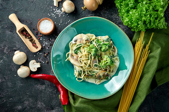 Spaghetti pasta with mushrooms, broccoli and white sauce in a plate on a dark background. Vegetarian pasta