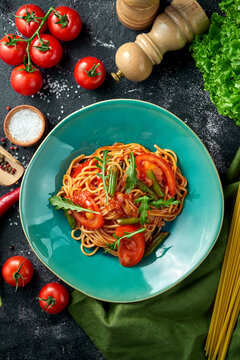 Pasta with tomatoes, asparagus and red sauce in a plate on a dark background.