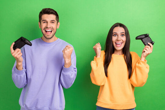 Photo of two delighted crazy people hold gamepad raise fist shout yes isolated on green color background