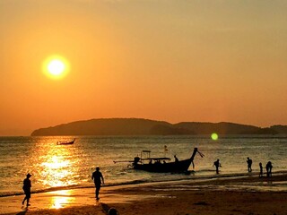 Fototapeta premium Beautiful tranquil sunset over the sea with fishermen long tail boat and few people dark silhouettes on the beach