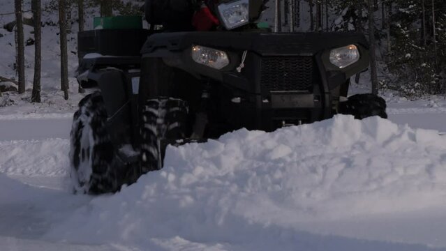 Ground level view of an ATV plowing snow and coming towards the camera