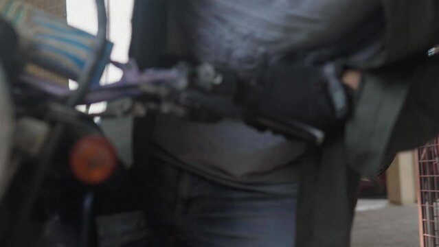 A man walks into an abandoned parking garage. Rode a dirt bike with sleeping bags attached on the front and back. 