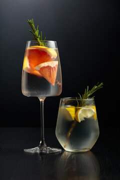 Gin tonic with ice, rosemary, lemon, and grapefruit on a black wooden table.