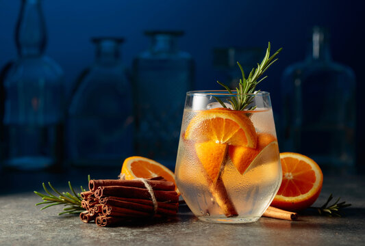 Cocktail gin tonic with ice, rosemary, cinnamon, and orange.