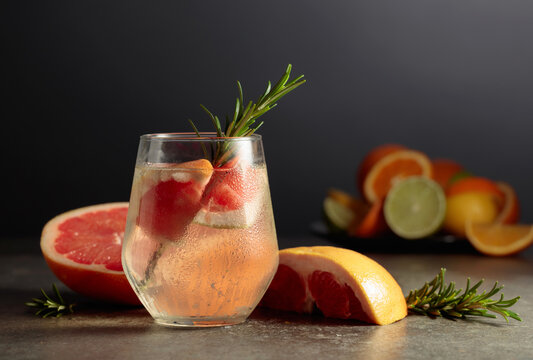 Cocktail gin tonic with ice, rosemary, and grapefruit on a stone table.