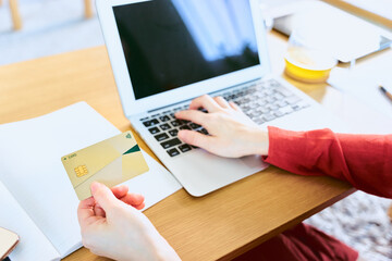 Fototapeta na wymiar クレジットカードでネットショッピングの買い物を決済する為にノートパソコンに番号を入力する女性の手元