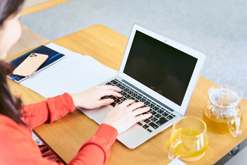 リビングのローテーブルにパソコンを広げキーボードでタイピングをして入力作業をする30代女性の手元