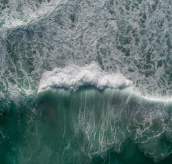 Aerial view of a wave in the ocean with surfers nearby