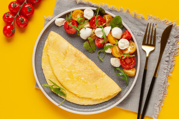 Salad with arugula, mozzarella and tomatoes in a plate on the table. Omelette with Caprese salad. Top view