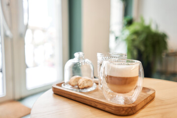 Cup of coffee cappuccino with cantuccini and a glass of water on a wooden tray. Coffee with milk, a cookie and a glass with water on a glass table.