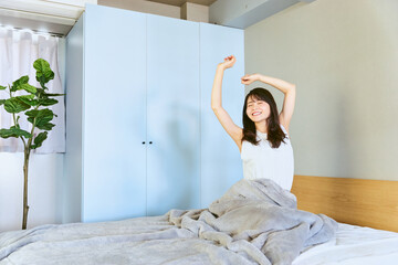 1人暮らしのベッドルームで休日の朝に快眠で目覚めた爽やかな気分の20代から30代の日本人の女性