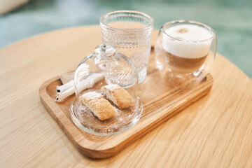 Cup of coffee cappuccino with cantuccini and a glass of water on a wooden tray. Coffee with milk, a...