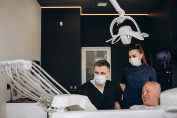 Young dentist and his assistant treating elderly man.