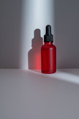 Red cosmetic bottle with pipette on white background with tonnel lit by the sun, product packaging, anti aging serum with peptides, cosmetics mockup, spa concept