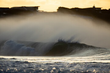 huge shore break wave breaking on a beach with a golden sunset