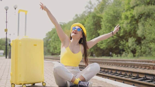 An exciting start to the journey. A suitcase, sunshine and waiting on the railway platform are all images of a happy young woman embarking on an exciting tourist vacation trip. On the railway platform