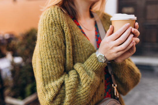 Female hands holding disposable coffee cup on urban background, close up, copy space. Drinking take away coffee. Breakfast on the go.