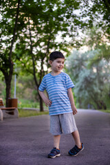 cute adorable boy in park photo shooting,in green grass,bench beside lake or brick wall or bridge.sunset golden hour.child at tree trunk or lying on straws.young model