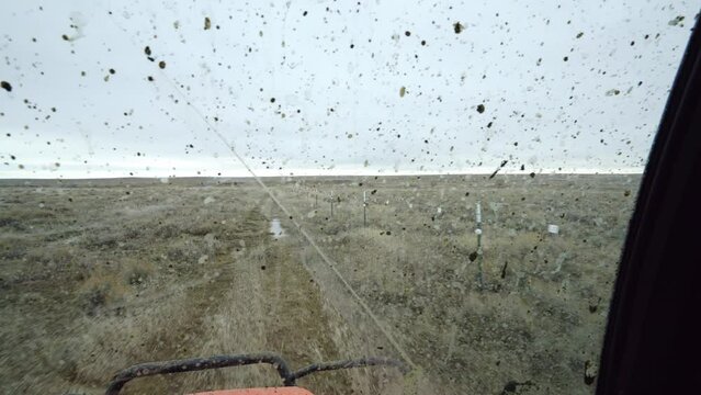 UTV driving fast along fence line on Montana prairie through muddy windshield