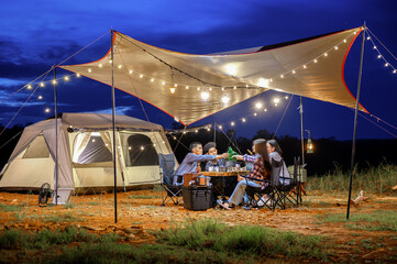 Outdoor camping tent in the forest park, party dinner with friends under tarp or flysheet and warm...