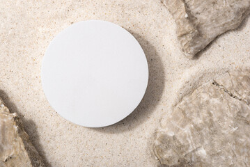 Natural cosmetic background for product presentation. Rocks and white podium on the sand. Top view.