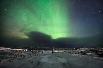 night landscape with northern lights and aurora by the sea in winter with a man in the frame