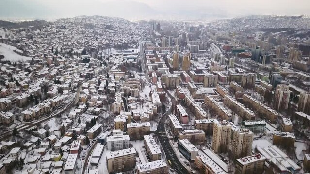 Aerial cinematic drone winter snowy streets and buildings downtown Sarajevo City center avaz twist Bosnia and Herzegovina cars and highway frozen landscape mid day slow pan up backward movement